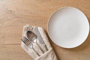 piatto vuoto o piatto con coltello, forchetta e cucchiaio su sfondo di piastrelle di legno foto
