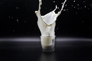 una fragola che cadeva in un bicchiere di latte ha causato schizzi di latte sullo sfondo nero foto