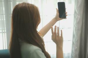 contento asiatico adolescente ragazza Tenere tampone computer aggeggio utilizzando digitale tavoletta tecnologia seduta su il divano a casa. sorridente giovane donna utilizzando app, shopping in linea, lettura notizia, navigazione Internet su divano foto