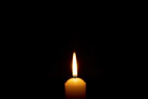 sfocato foto di singolo ardente candela fiamma o leggero raggiante su un' grande giallo candela su nero o buio sfondo su tavolo nel Chiesa per Natale, funerale o memoriale servizio con copia spazio.
