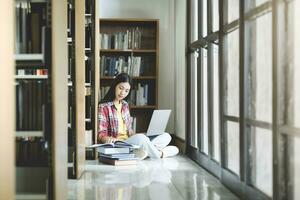 giovane Università alunno utilizzando il computer portatile per in linea apprendimento, ricerca e apprendimento a biblioteca. foto