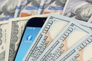 smartphone schermo con Facebook App e lotto di centinaio dollaro fatture. attività commerciale e sociale networking concetto foto