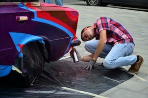 Kharkov, Ucraina - Maggio 27, 2017 Festival di strada arte. giovane ragazzi disegnare graffiti su il auto corpo nel il città centro. il processi di disegno colore graffiti su un' auto con aerosol lattine foto