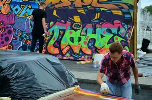 Kharkov, Ucraina - Maggio 27, 2017 Festival di strada arte. giovane ragazzi disegnare graffiti su il auto corpo nel il città centro. il processi di disegno colore graffiti su un' auto con aerosol lattine foto