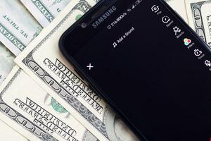 smartphone schermo con tic toc App e lotto di centinaio dollaro fatture. attività commerciale e sociale networking concetto foto