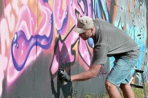 giovane caucasico maschio graffiti artista disegno grande strada arte pittura nel blu e rosa toni foto