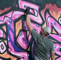 giovane caucasico maschio graffiti artista disegno grande strada arte pittura nel blu e rosa toni foto