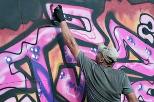 giovane caucasico maschio graffiti artista disegno grande strada arte pittura nel blu e rosa toni foto