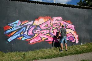 giovane caucasico maschio graffiti artista disegno grande strada arte pittura nel blu e rosa toni foto