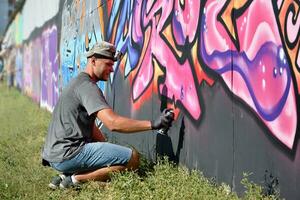 giovane caucasico maschio graffiti artista disegno grande strada arte pittura nel blu e rosa toni foto