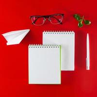 forniture per ufficio su uno sfondo rosso. quaderno bianco, penna e occhiali. layout per il design nello stile del minimalismo.