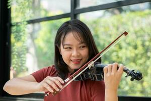 un attraente donna apprendimento musicista giochi il violino a casa. compositore la creazione di canzoni con corda strumenti. sognante violinista dita urgente stringhe su violino foto