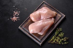 filetto di pollo fresco su un tavolo di cemento scuro con spezie ed erbe aromatiche foto