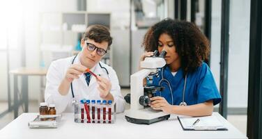 focalizzata maturo maschio medico e africano femmina infermiera Guarda a tavoletta e il computer portatile discutere anamnesi insieme. concentrato diverso medico professionisti nel Ospedale. foto