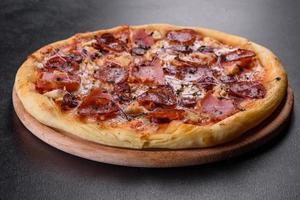 deliziosa pizza fresca al forno con pomodori, salame e pancetta su uno sfondo di cemento scuro foto