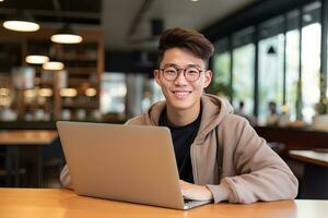 ritratto di allegro maschio alunno apprendimento in linea nel caffè negozio, giovane asiatico uomo studi con il computer portatile nel bar, fare compiti a casa foto