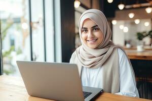 ritratto di bellissimo musulmano femmina alunno in linea apprendimento nel caffè negozio, giovane donna con hijab studi con il computer portatile nel bar, ragazza fare sua compiti a casa foto