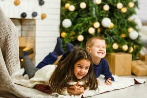contento poco bambini decorare Natale albero nel bellissimo vivente camera con tradizionale fuoco posto. bambini apertura regali su natale vigilia. foto