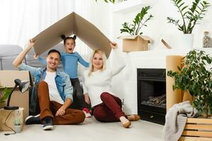 contento famiglia seduta su di legno pavimento. padre, madre e bambino avendo divertimento insieme. in movimento Casa giorno, nuovo casa e design interno concetto foto