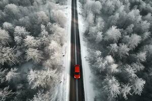 aereo Visualizza di un' rosso auto su un' nevoso strada passaggio attraverso un' inverno foresta, generativo ai foto