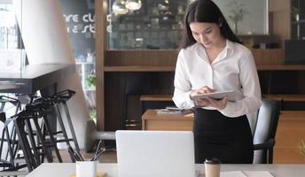 ritratto di giovane donna d'affari in piedi alla sua scrivania utilizzando un laptop foto
