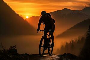 silhouette di un' viaggiatore su un' montagna bicicletta nel il arancia leggero di il crescente sole contro il fondale di un' montagna paesaggio foto