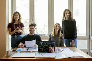 ritratto di quattro contento studenti a scrivania e a il finestra foto