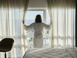 donna apertura bianca tenda mentre guardare attraverso finestra a lusso Hotel camera foto