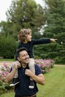 contento padre trasporto figlio su le spalle nel parco foto