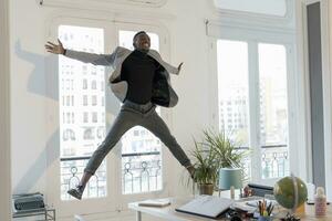 contento giovane uomo d'affari salto nel il aria nel il suo ufficio foto