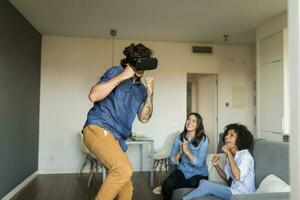 Due donne incoraggiando uomo gioco con vr bicchieri a casa foto