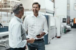 maturo uomo d'affari Tenere inteligente Telefono mentre discutere con collega nel industria foto