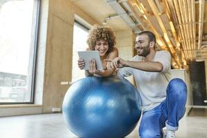 contento uomo e donna utilizzando tavoletta su fitness palla nel moderno ufficio foto