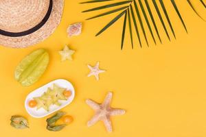 carambola di frutta, accessori da spiaggia e fogliame di una pianta tropicale su carta colorata foto