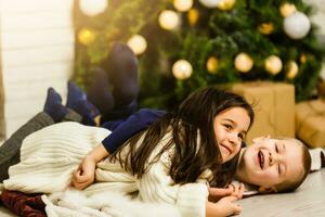 famiglia su Natale vigilia a il camino. bambini sotto Natale albero con regalo scatole. decorato vivente camera con tradizionale fuoco posto. accogliente caldo inverno sera a casa. foto