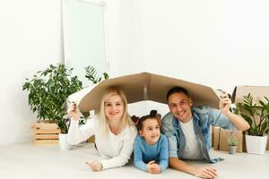 contento famiglia seduta su di legno pavimento. padre, madre e bambino avendo divertimento insieme. in movimento Casa giorno, nuovo casa e design interno concetto foto