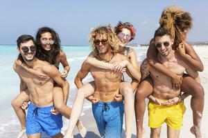 amici a piedi su il spiaggia, trasporto amiche a cavalluccio foto