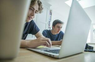 Due adolescenziale ragazzi utilizzando il computer portatile e tavoletta su tavolo a casa foto