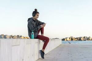 allegro giovane donna con cuffie durante allenamento, utilizzando smartphone foto