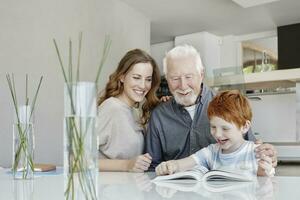 contento nonno, madre e figlio lettura libro nel un' villa foto