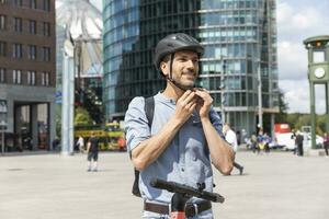 uomo fissaggio il casco prima equitazione su elettrico scooter, Berlino, Germania foto