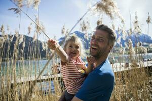 Austria, tirolo, Walchsee, contento padre trasporto figlia nel canne a il sponde del lago foto