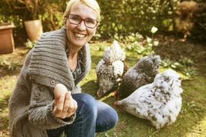 ritratto di contento donna nel giardino con sua orpington galline mostrando uovo foto