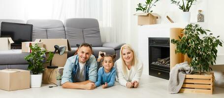 contento famiglia seduta su di legno pavimento. padre, madre e bambino avendo divertimento insieme. in movimento Casa giorno, nuovo casa e design interno concetto foto