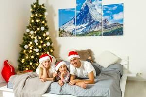 contento giovane famiglia bugie su letto nel Camera da letto a Natale e sorridente a telecamera foto