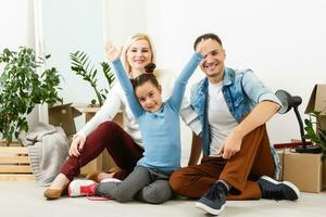 contento famiglia seduta su di legno pavimento. padre, madre e bambino avendo divertimento insieme. in movimento Casa giorno, nuovo casa e design interno concetto foto