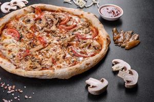 pizza italiana fresca e deliziosa con funghi e pomodori su uno sfondo di cemento scuro foto