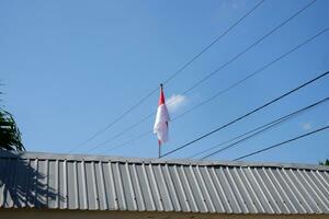 il rosso e bianca indonesiano bandiera è volante contro un' sfondo di blu cielo e cavi foto