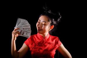 ritratto donna asiatica vestito rosso tradizionale cheongsam azienda denaro 100 dollari americani a sfondo nero foto