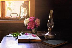 natura morta di oggetti vintage e un bouquet di peonie su un tavolo vicino alla finestra in una vecchia casa di paese. foto